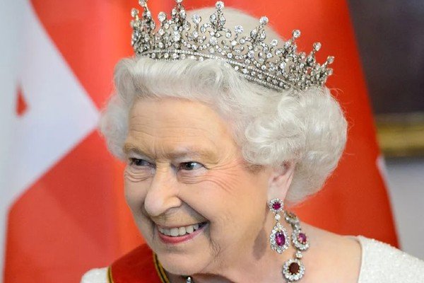 Na photography color, a rain Elizabeth aparece no centro in image sorrindo utilizando a coroa real